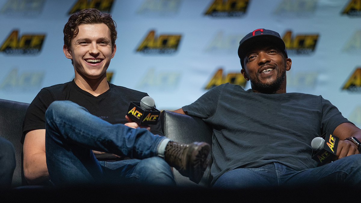 Tom Holland and Anthony Mackie sitting, laughing, holding microphones at a panel event