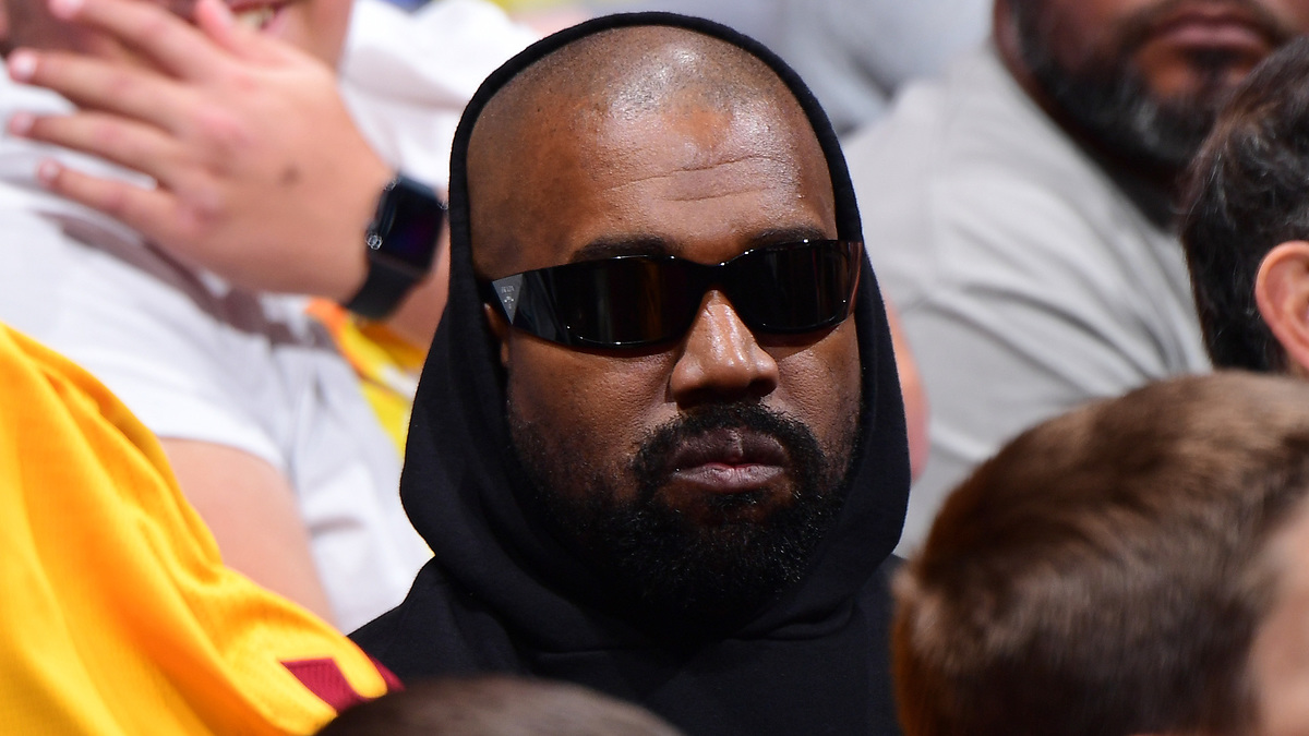 Man in black hoodie and sunglasses sitting among a crowd