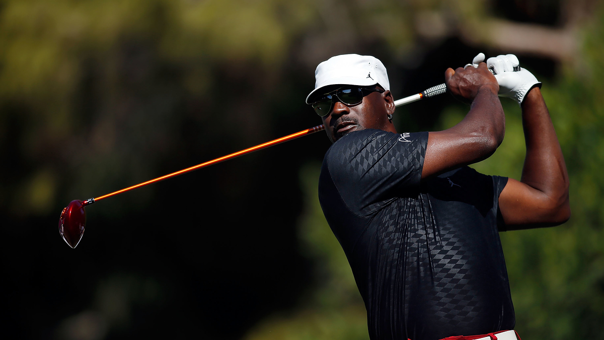 Golfer in mid-swing with driver on course, wearing cap, sunglasses, and a fitted shirt