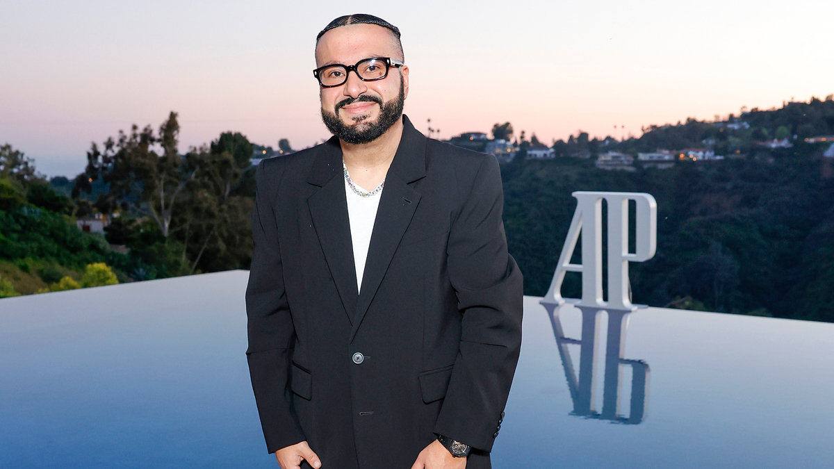 Music artist in black suit stands before event backdrop with letters "AP" visible