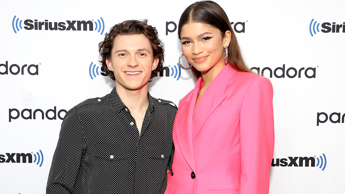 Two individuals smiling for the camera, one in a patterned shirt, the other in a pink blazer