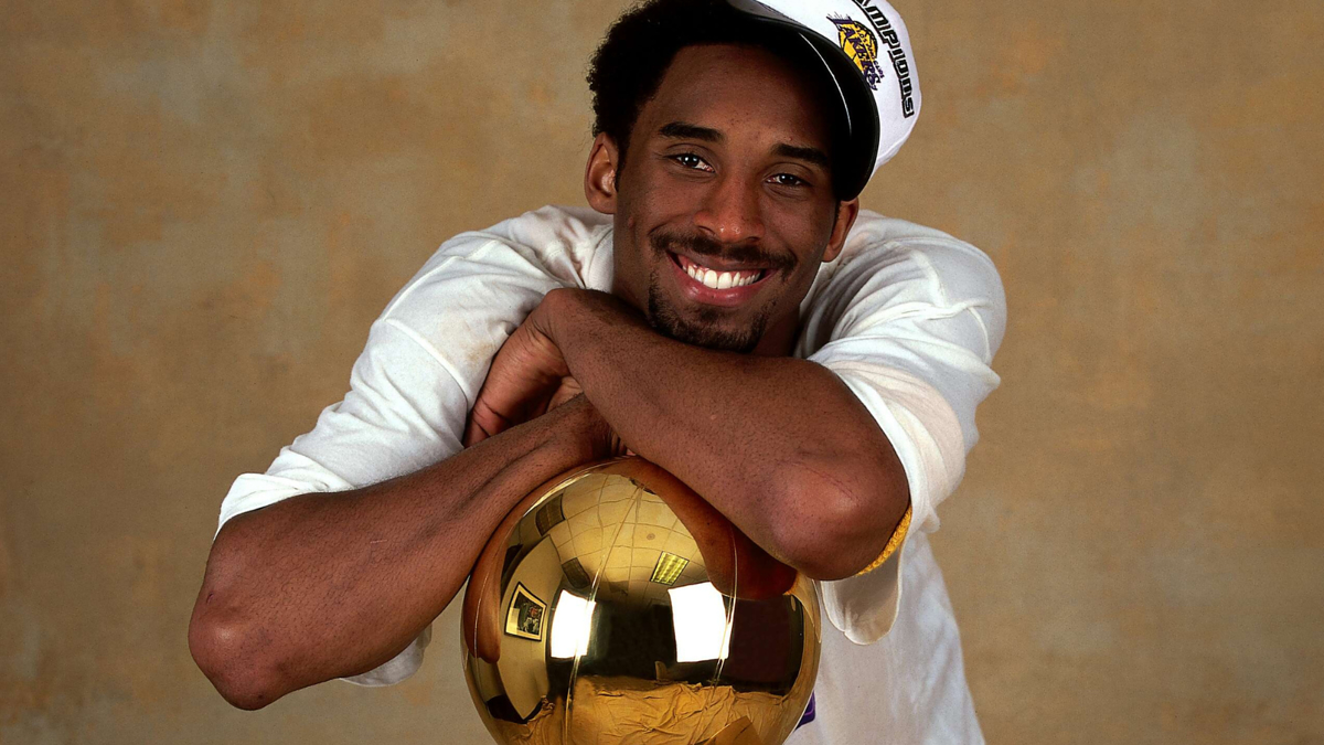 Smiling person holding a shiny basketball trophy, wearing a white top and championship cap