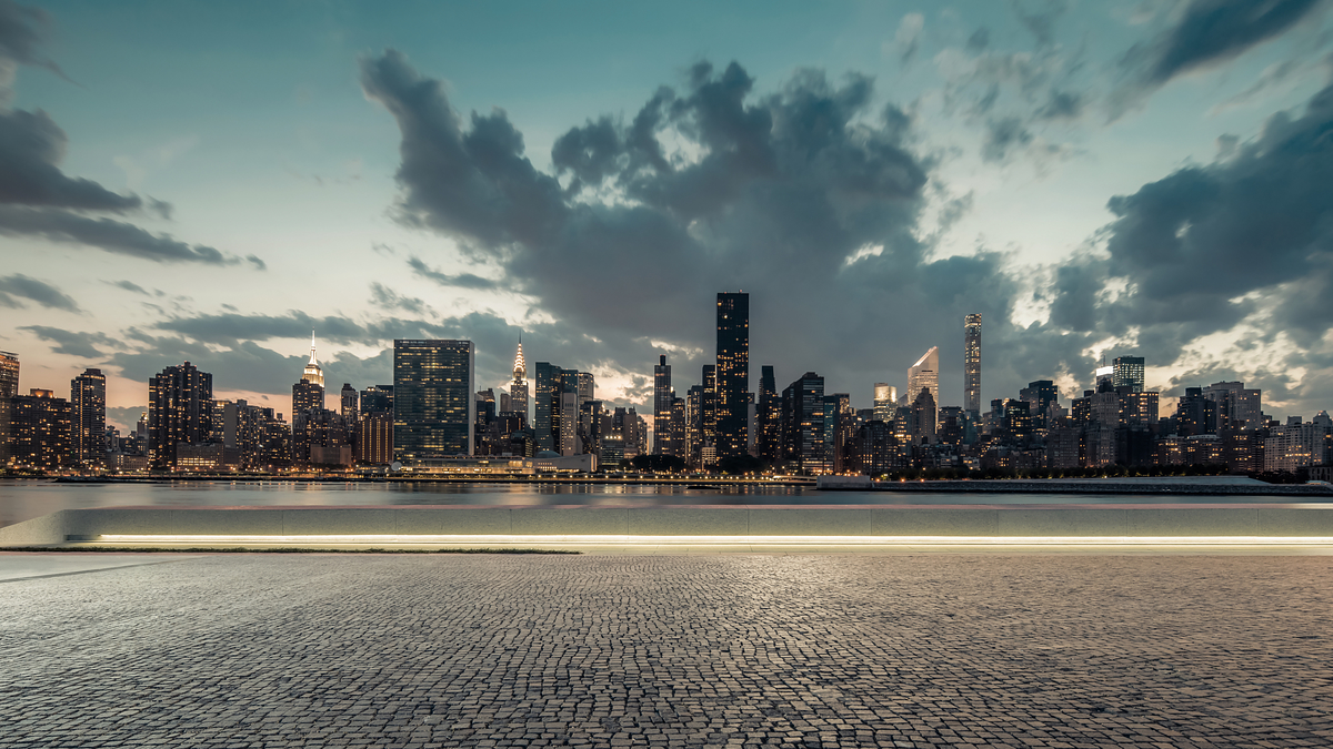 City skyline viewed from a cobblestone waterfront at dusk, no people visible