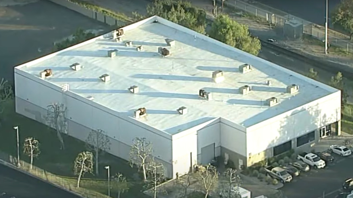 Aerial view of a large industrial building with a flat roof and parked cars nearby