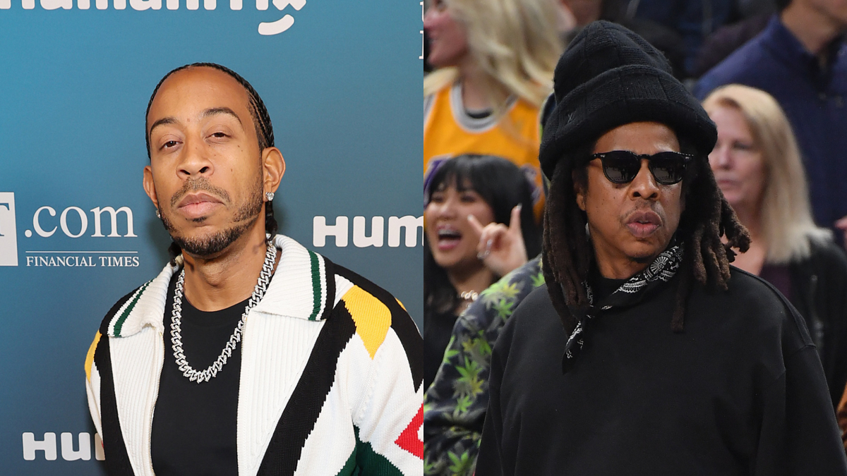 Two men at an event; one wears a striped cardigan and chain, and the other sports a black hat and layered shirts