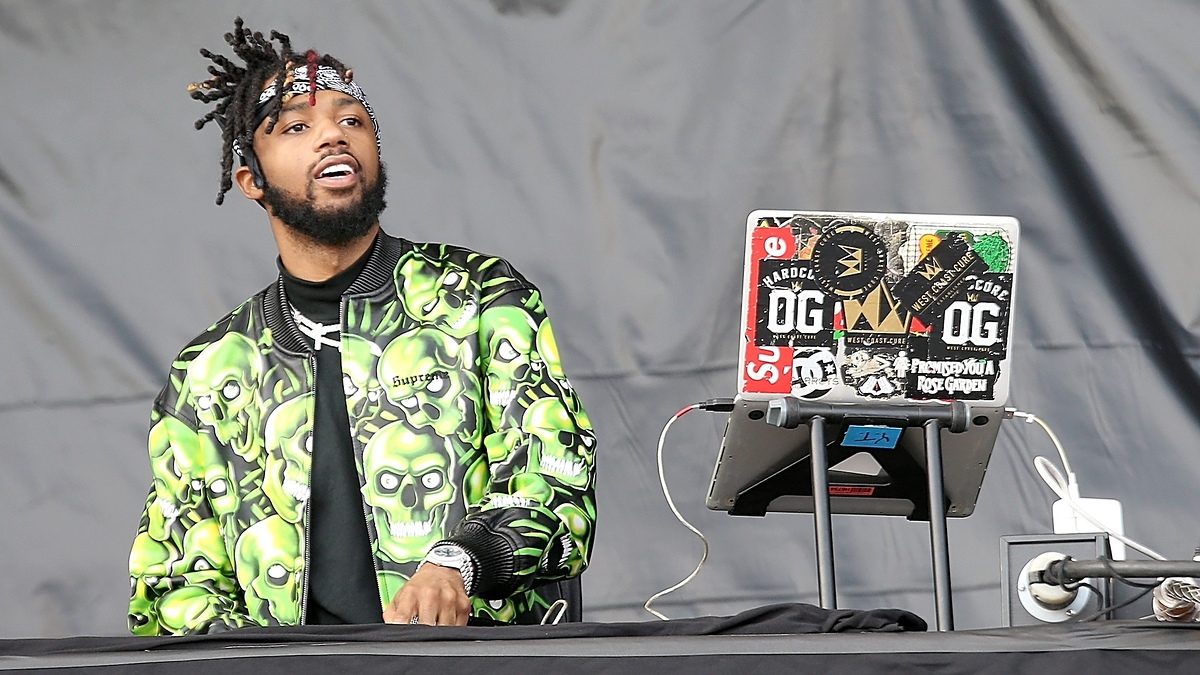 DJ at a mixing table wearing a jacket with skull patterns and headphones around neck