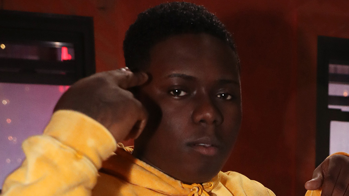 Person in a yellow hoodie adjusting their earring, intense gaze towards the camera