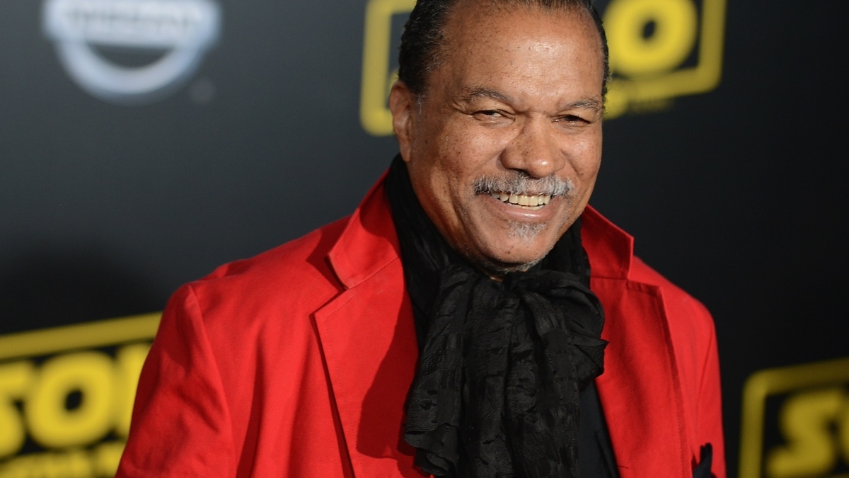 Smiling person in a red jacket and ruffled black scarf at an event