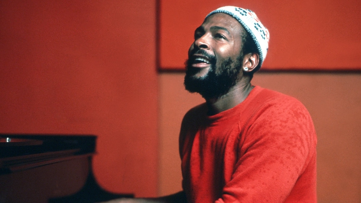 Marvin Gaye wearing a beanie and red sweater, singing passionately with a piano in the background