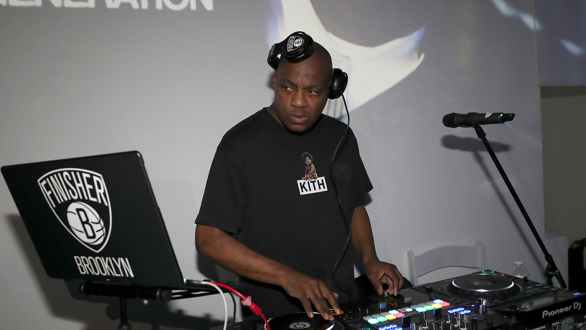 DJ at equipment focusing on mixing music with logo on laptop and wearing a branded t-shirt
