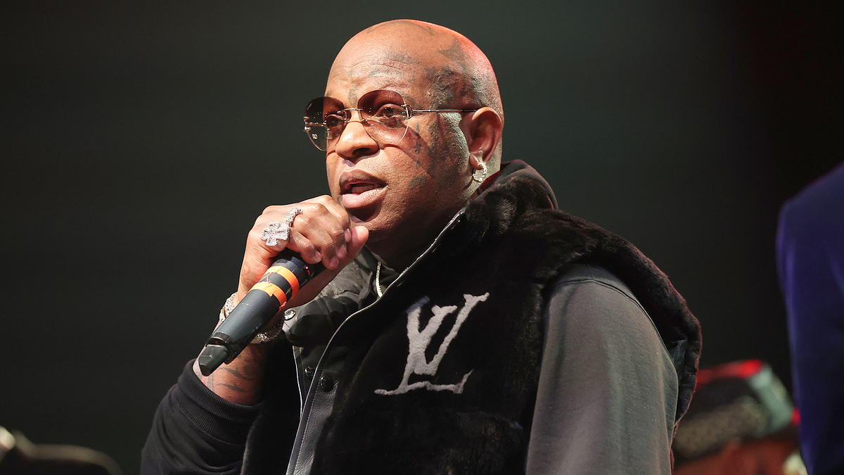 Music artist performing on stage with a microphone, wearing a logo sweater and glasses