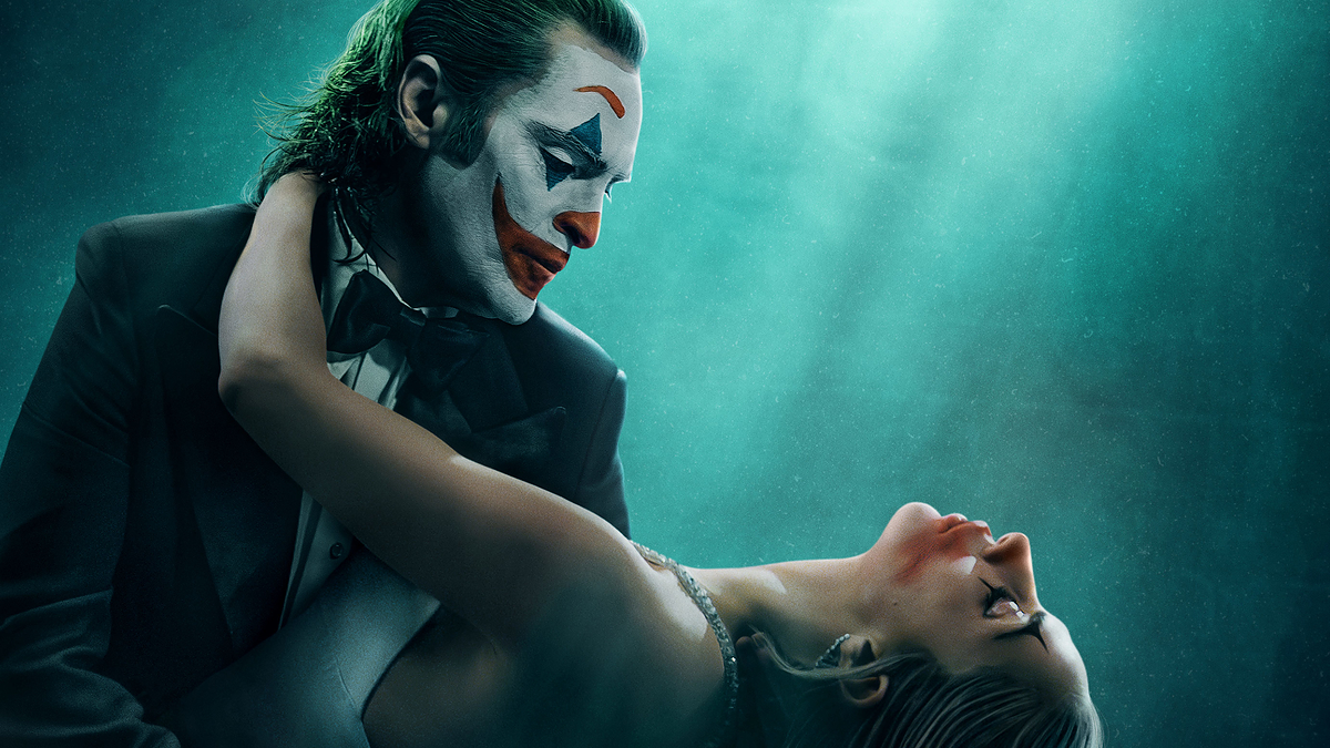 Promotional poster for 'Joker' featuring Joaquin Phoenix in makeup, embracing Lady Gaga as Harley Quinn, with spotlight above
