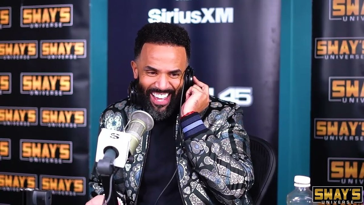 Man in patterned jacket laughing at SiriusXM studio with microphone and logo in the background