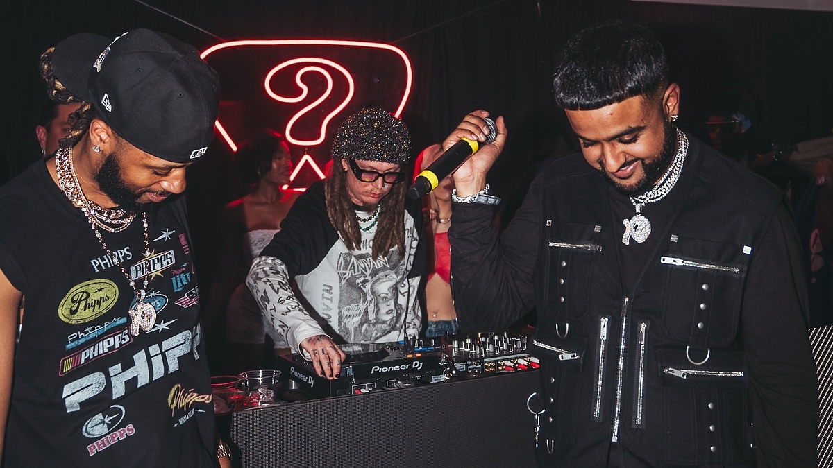 Three DJs at a mixing console with one actively adjusting equipment