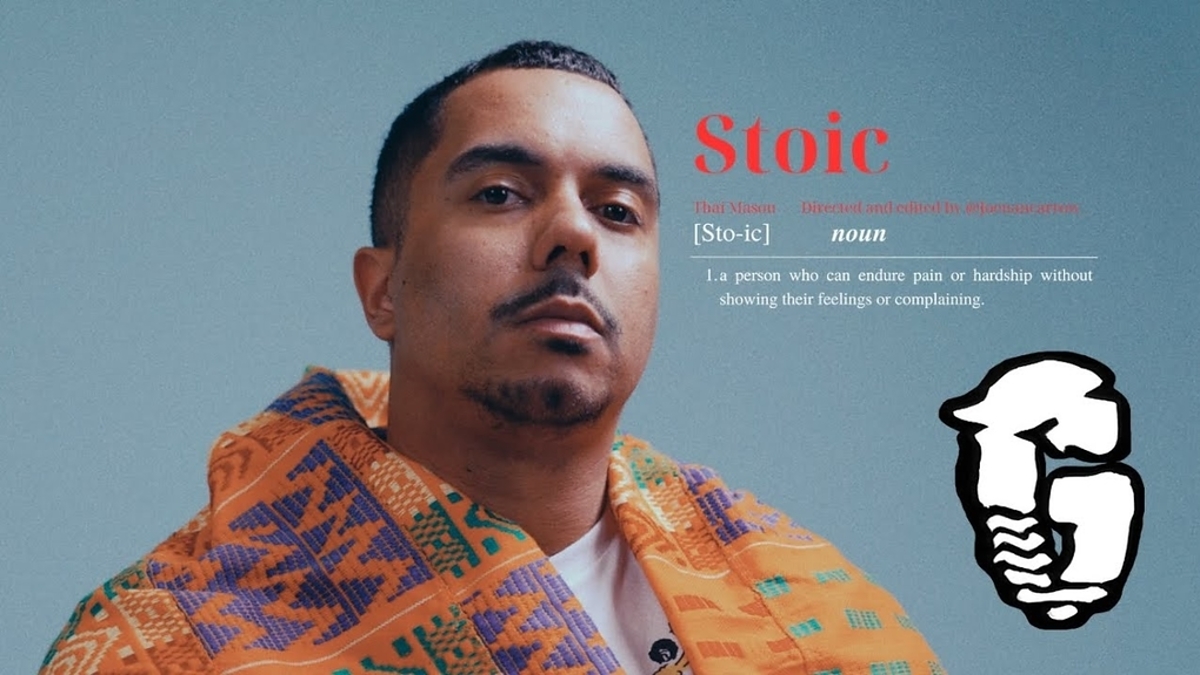 An artist poses with a stoic expression, wearing a patterned jacket; the definition of 'stoic' is displayed next to him