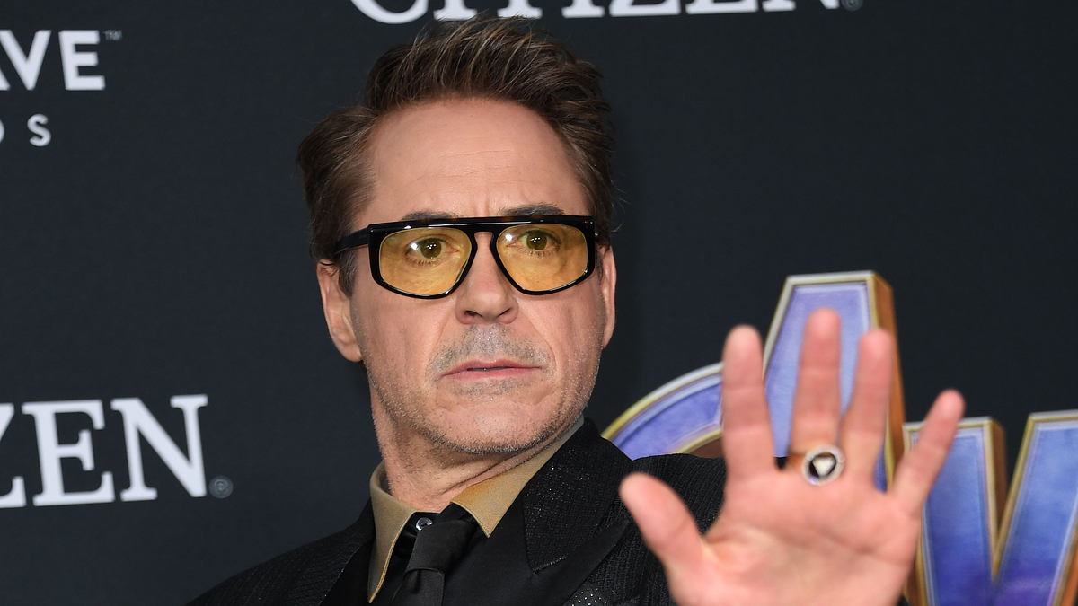 Robert Downey Jr. raising his hand, wearing glasses and a suit at an event
