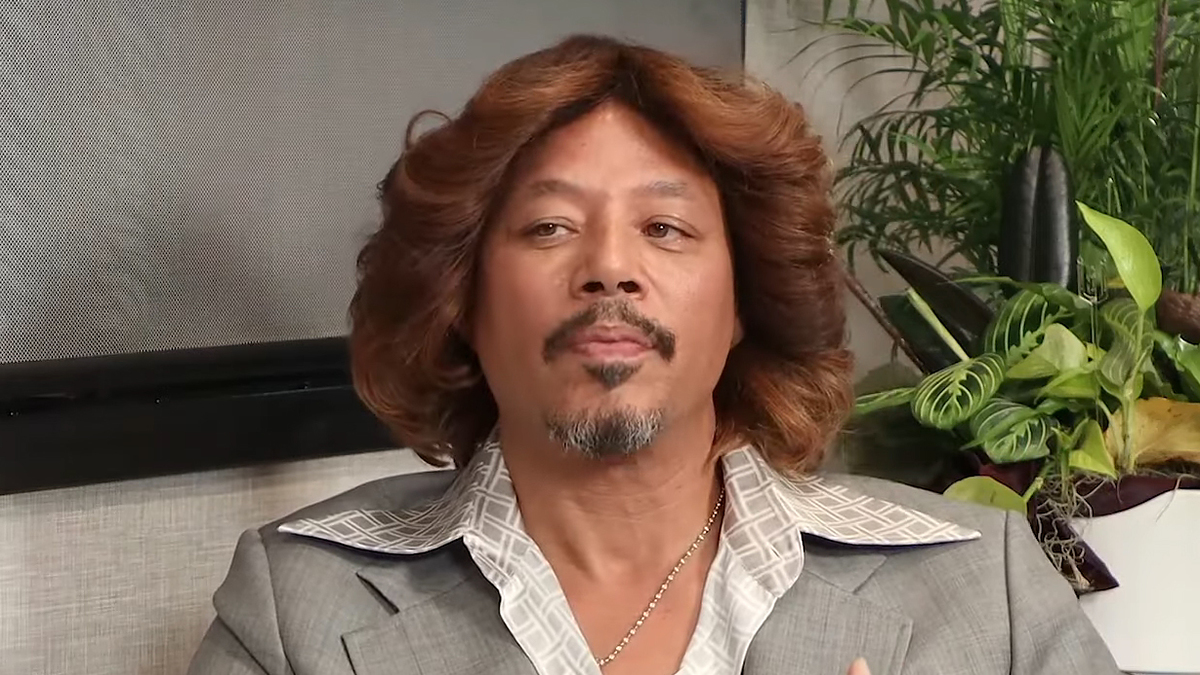 Man with medium-length wavy hair sitting, wearing a striped suit jacket and a patterned shirt