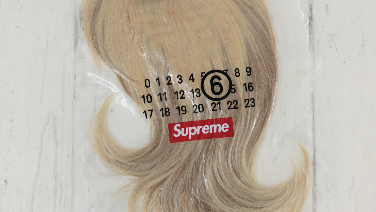 Blonde wig on a numbered guide chart with "Supreme" logo, displayed on a wooden floor