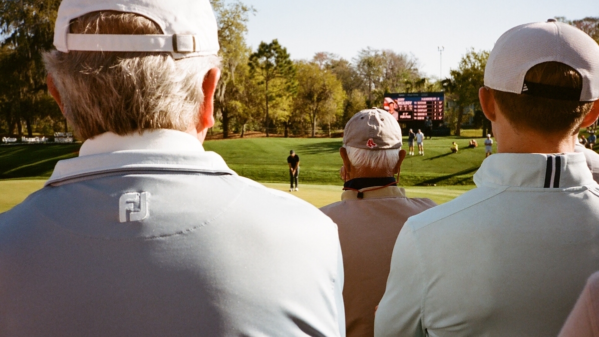 Three spectators in casual attire watching a golfer in the distance at a golf tournament