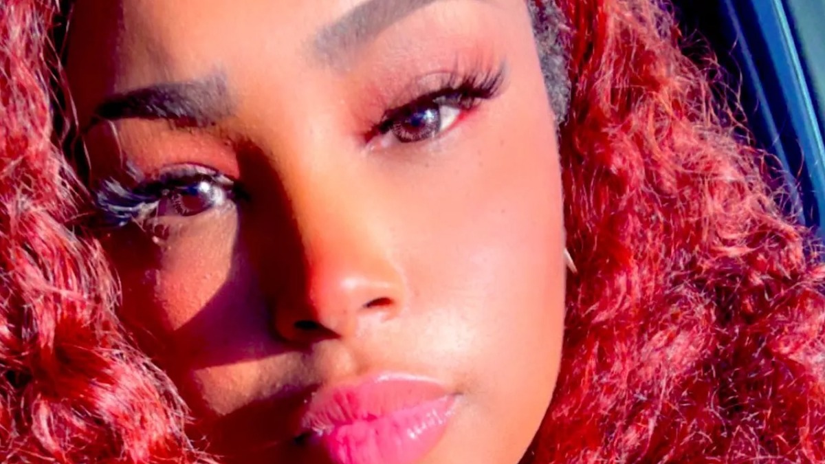 Close-up of a person with voluminous curly hair, full lashes, and glossy lips