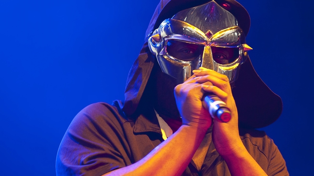 Performer on stage wearing a distinctive mask and holding a microphone