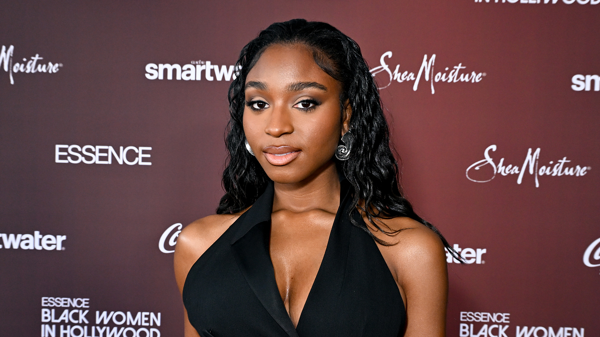 Normani in a black outfit posing at an event. She wears hoop earrings and has her hair down