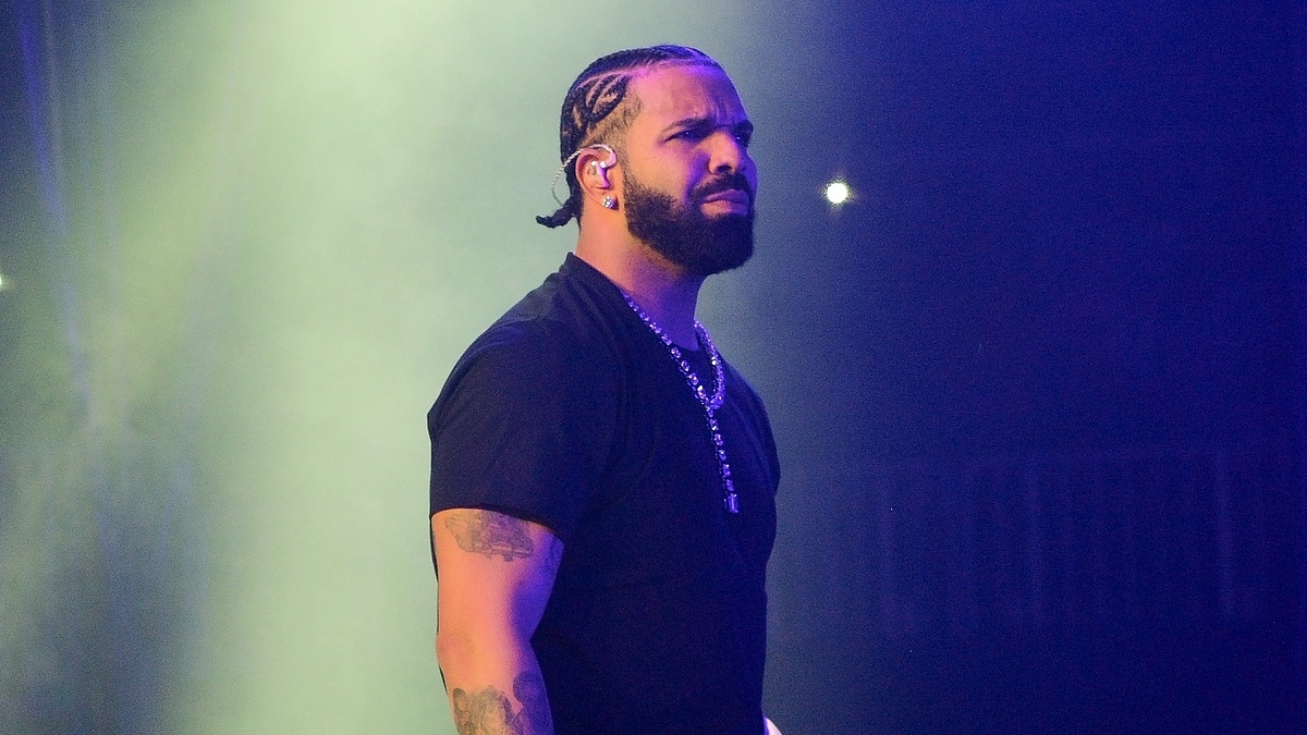 Drake on stage performing, wearing a casual outfit with a short-sleeved shirt