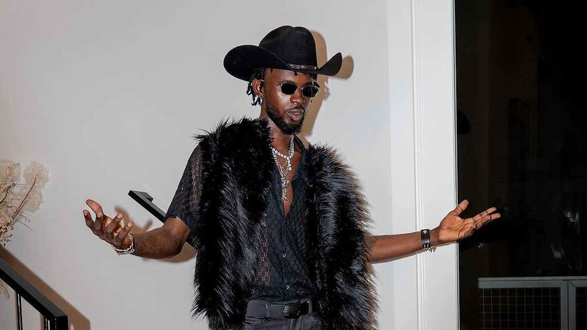 Music artist in a cowboy hat and fur vest posing with hands outstretched