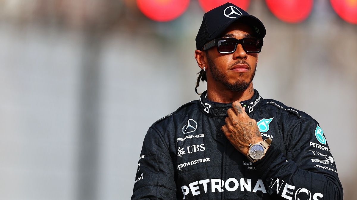 Lewis Hamilton in a racing suit, standing confidently with hand on heart