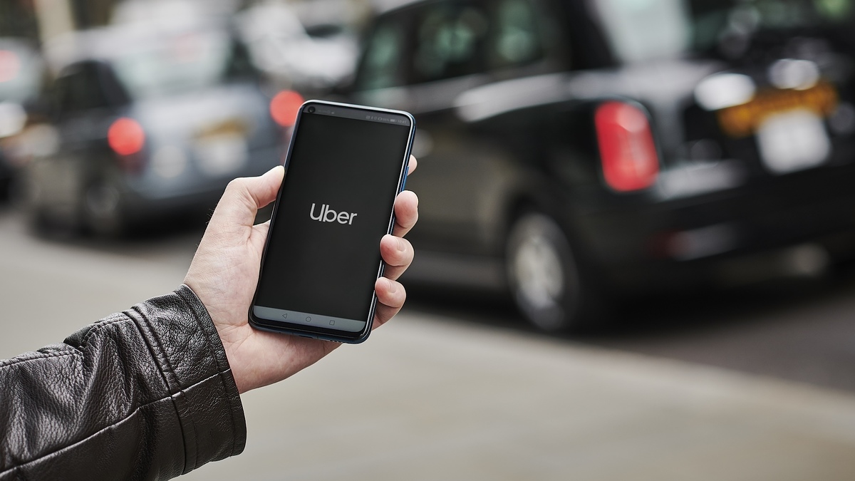 Hand holding smartphone with Uber app on screen, black cab in the background