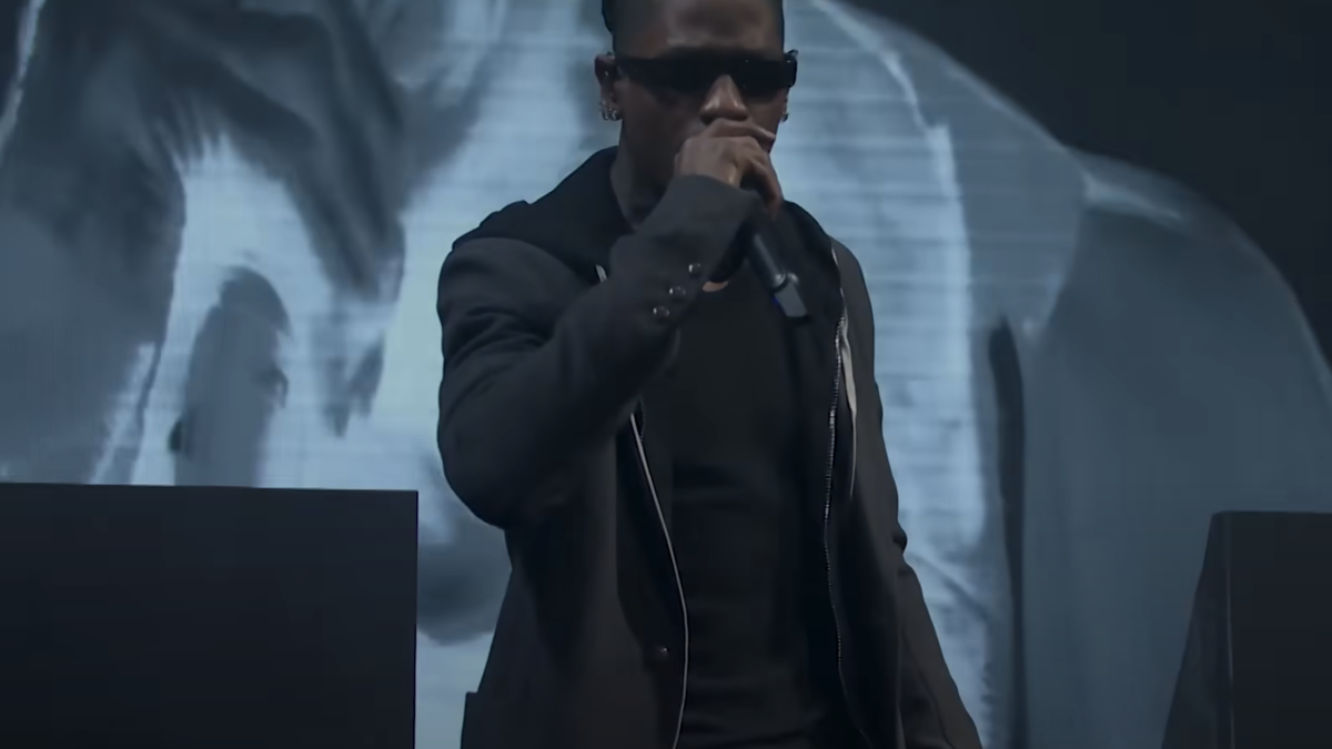 Music artist performing on stage with microphone and graphic backdrop