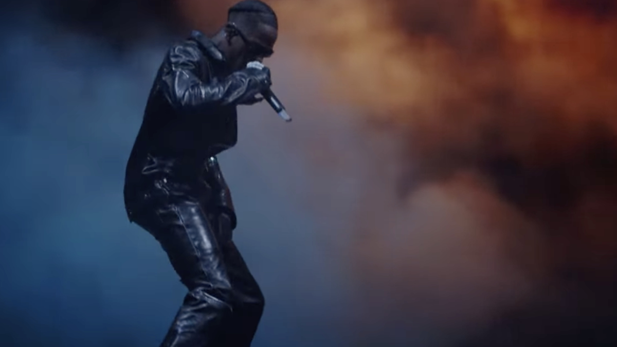 Music artist in a metallic outfit performs on stage with a microphone