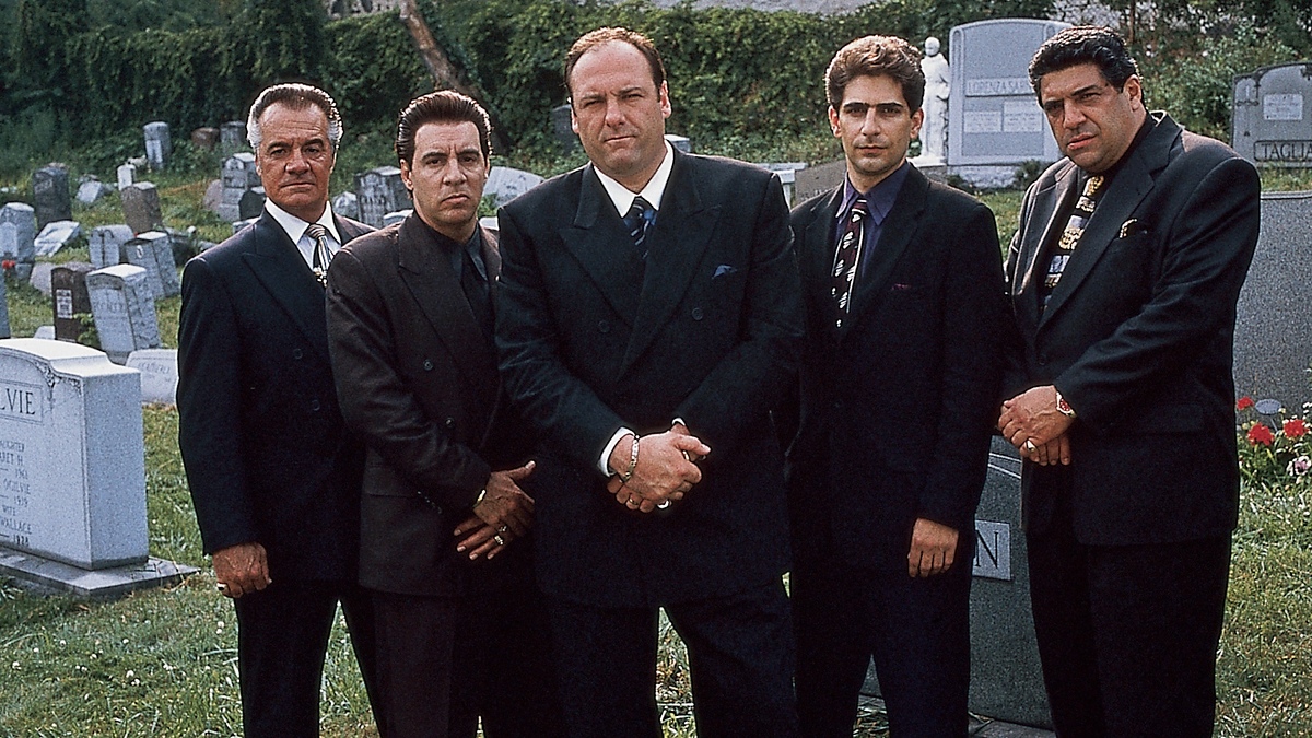 Five men dressed in dark suits and ties standing solemnly in a cemetery