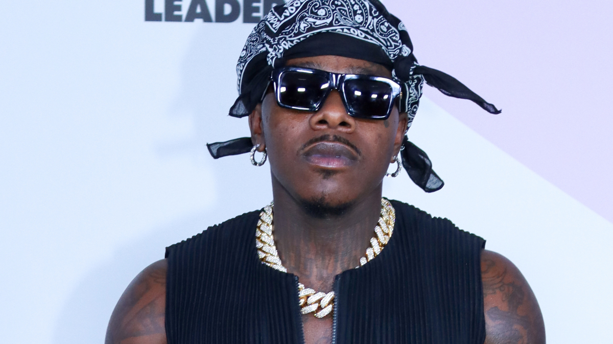 Man wearing a bandana, sleeveless shirt and necklaces posing at an event