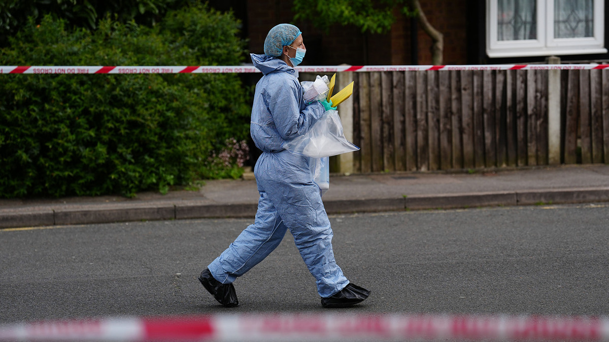 Person in protective gear walking by a taped-off area, carrying items