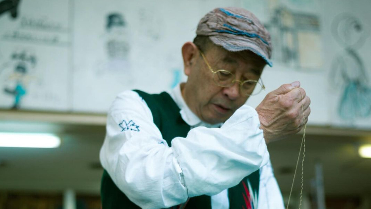Craftsman examining a string in workshop, wearing a cap and vest