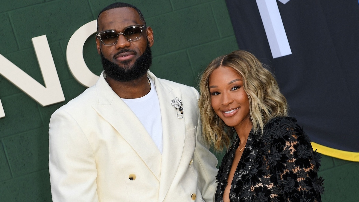 LeBron James in a white suit with a brooch next to a person in a black floral outfit