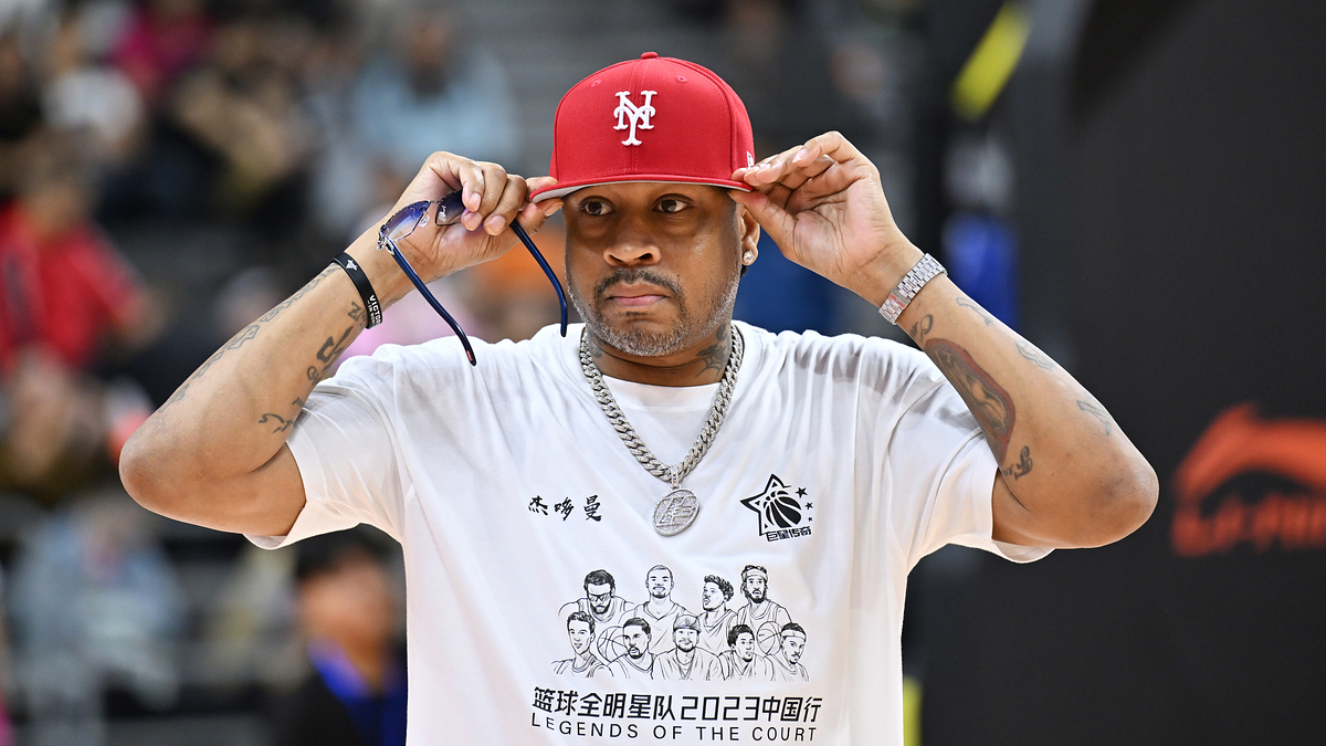 Person adjusting a baseball cap, wearing a T-shirt with a graphic design, at a sports event