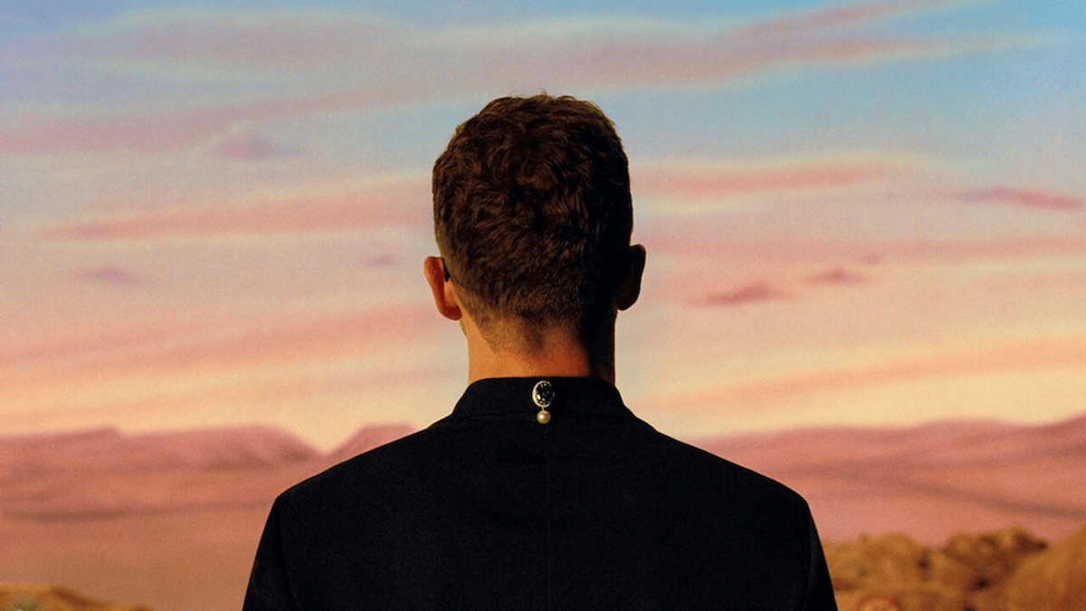 Person facing away, wearing a black jacket, with a desert and sunset backdrop