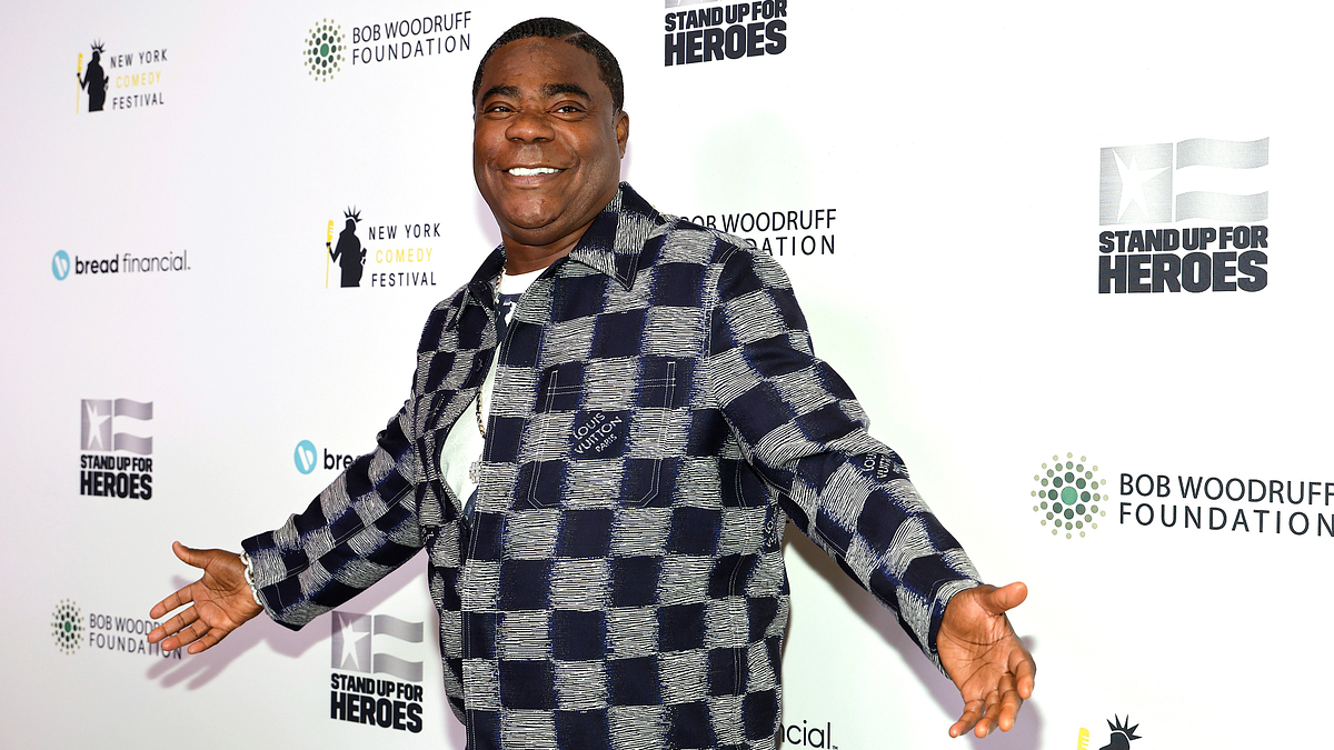 Tracy Morgan in a checkered jacket and pants standing with arms open wide at a Stand Up for Heroes event