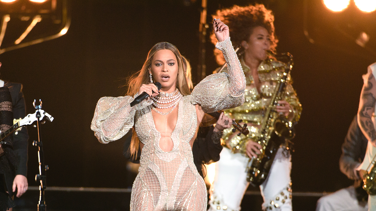 Beyoncé performing on stage in a sparkling bodysuit with musicians, including a guitarist
