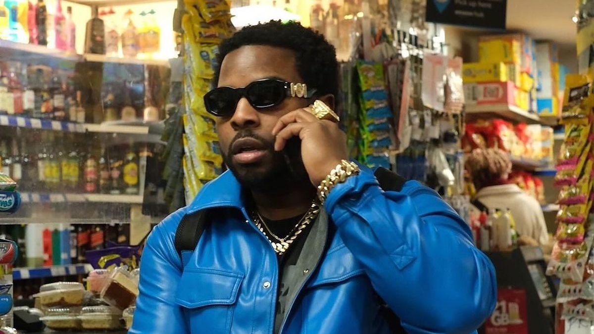 Man in a blue jacket and sunglasses on a phone in a convenience store.