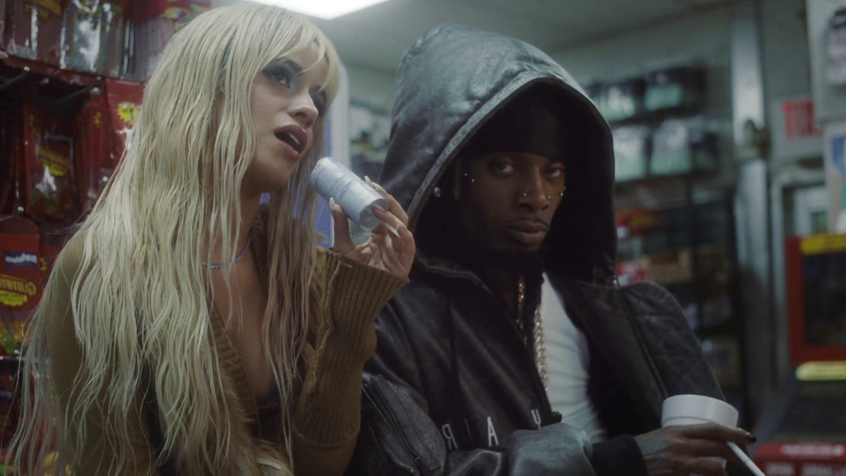 Two individuals posing together inside a store, one holding a beverage cup and the other with a microphone