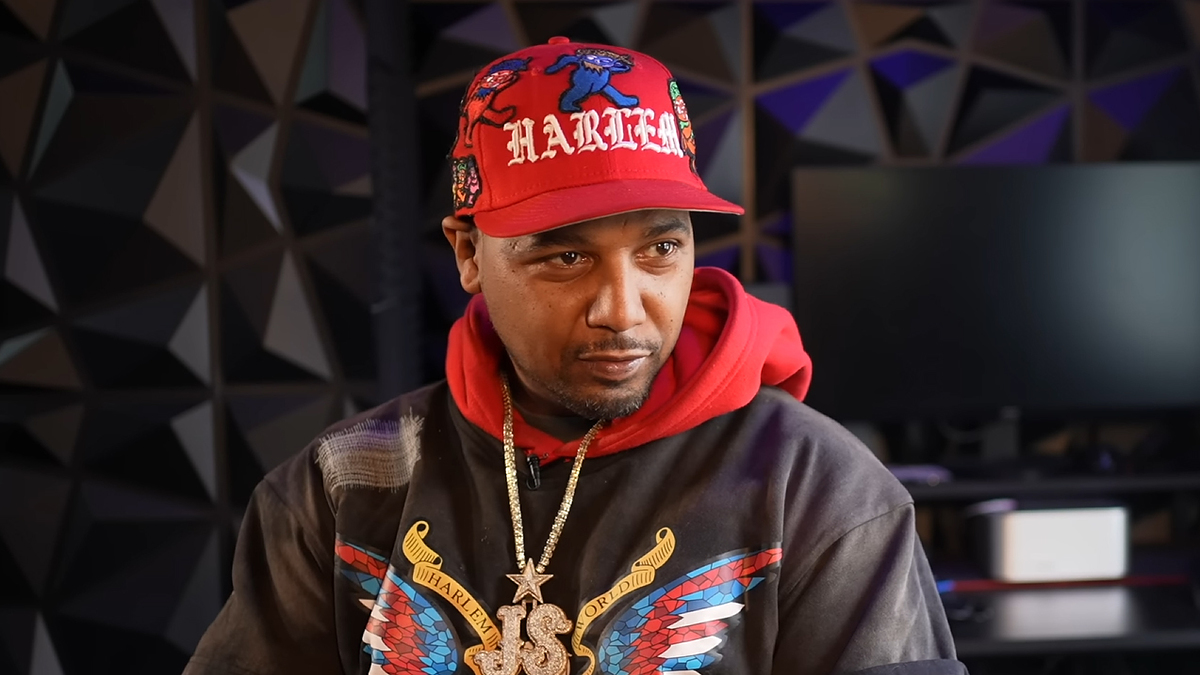 Man in a baseball cap and hoodie featuring graphics, with a prominent chain necklace