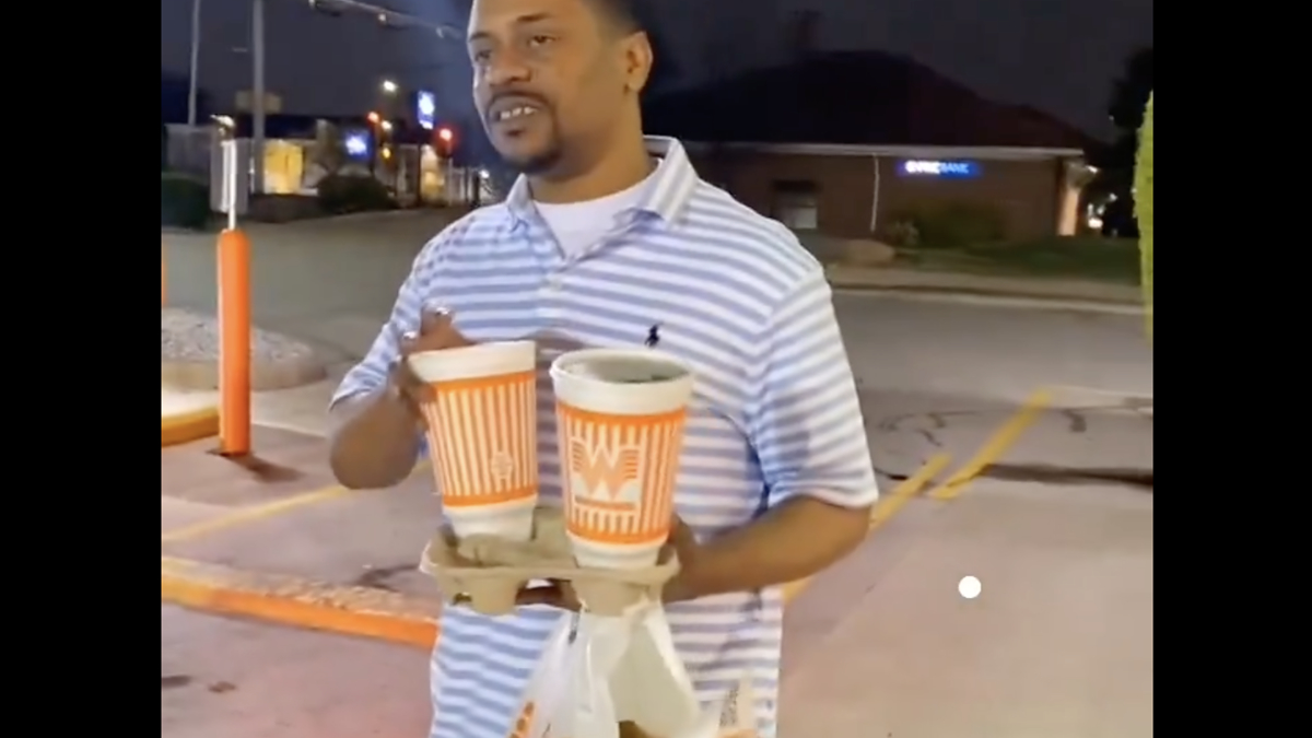 Man holding a cup and food bags outside, likely from a fast-food restaurant