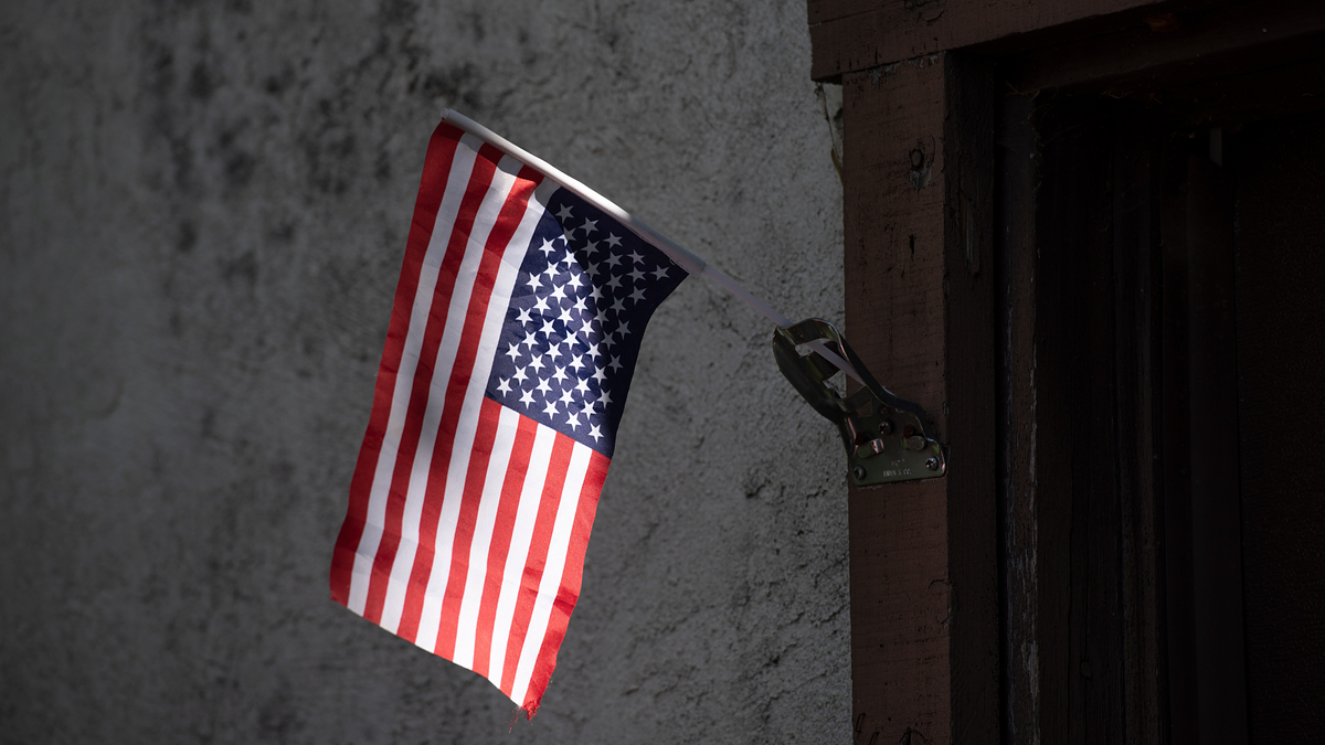An American flag hangs from a metallic bracket on a textured wall