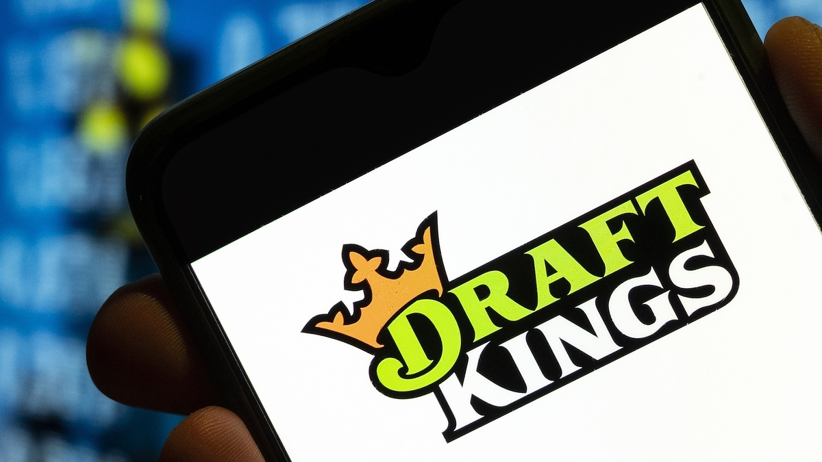 Hand holding smartphone displaying DraftKings logo with blurred digital screen in the background