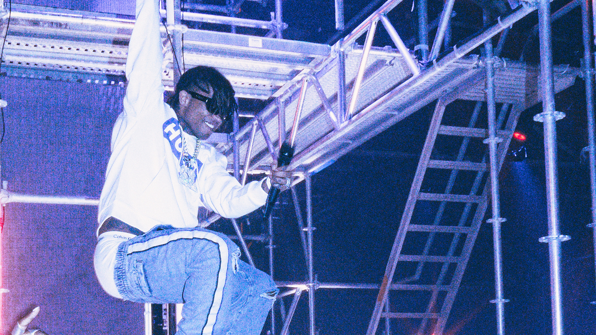 Performer in mid-air above crowd, casual attire, during a lively concert