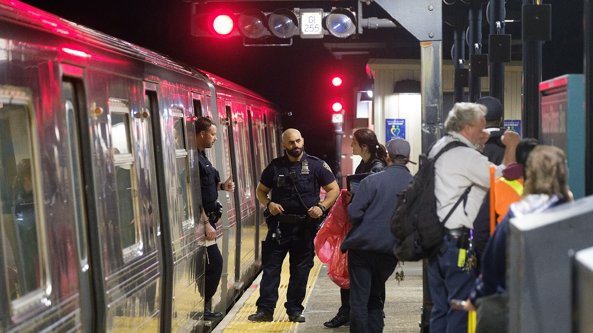 Police officer and passengers at a train station platform with open train doors