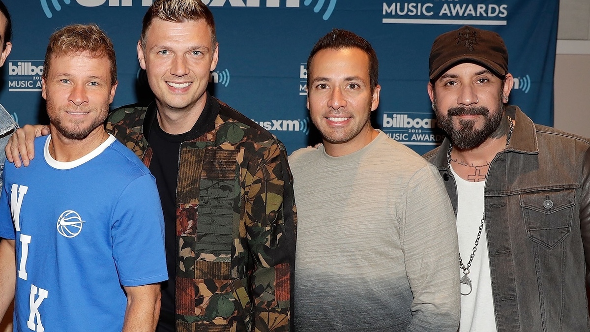 Backstreet Boys posing together at a SiriusXM event, smiling in casual wear with a backdrop featuring logos